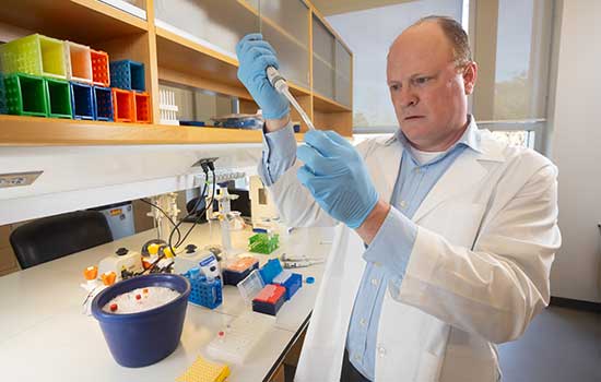 Professor in white lab coat holding up syringe in lab.