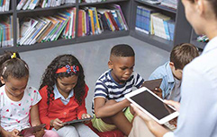 Teacher working with children in the library with ipads.